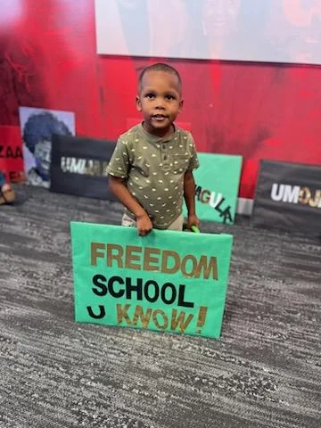 A young child holding a Freedom School sign